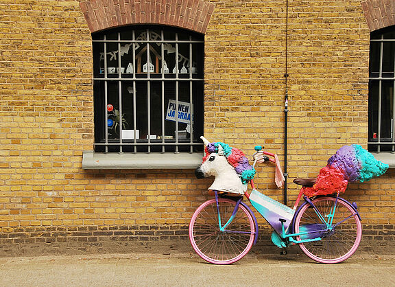 Ein Fahrrad, an dem aus Pappmache ein Einhorn-Kopf und Einhorn-Schweif befestigt sind.
